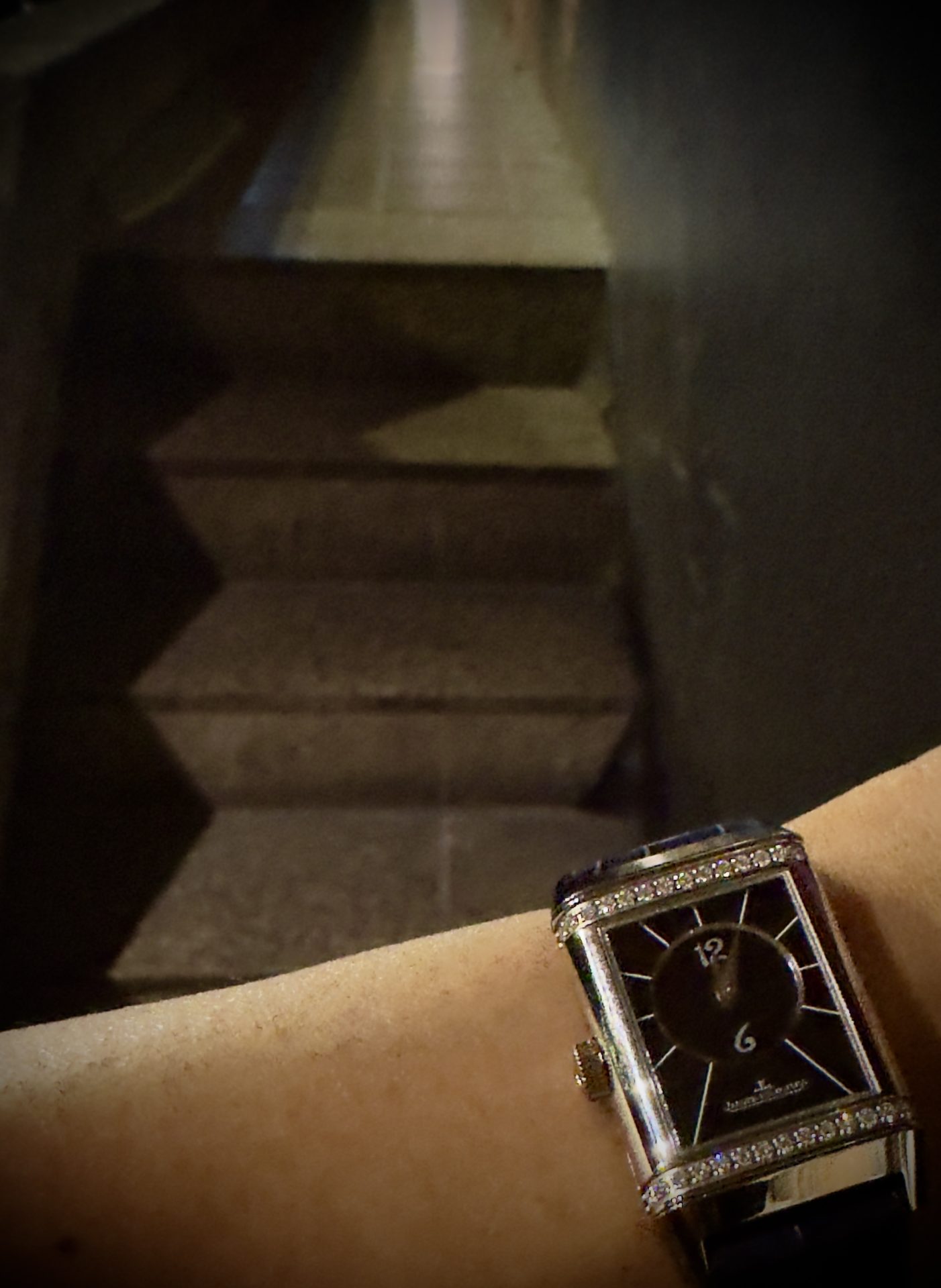 Jaeger-LeCoultre Reverso with black dial and diamond-set case, photographed in warm evening light against a bronze backdrop.