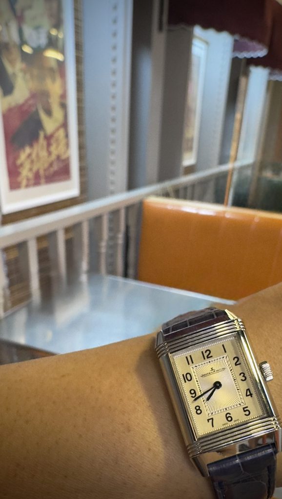 Jaeger-LeCoultre Reverso with cream dial and black strap, captured at a Sydney café table beside a yellow booth. 