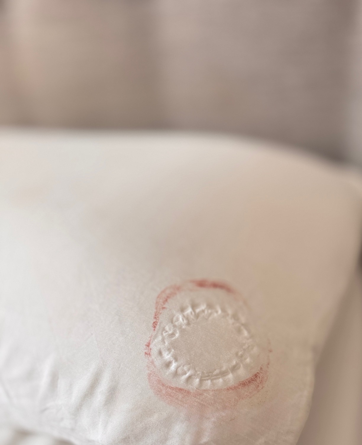 White pillow with faint lipstick-stained bite mark, hinting at intimacy and playfulness