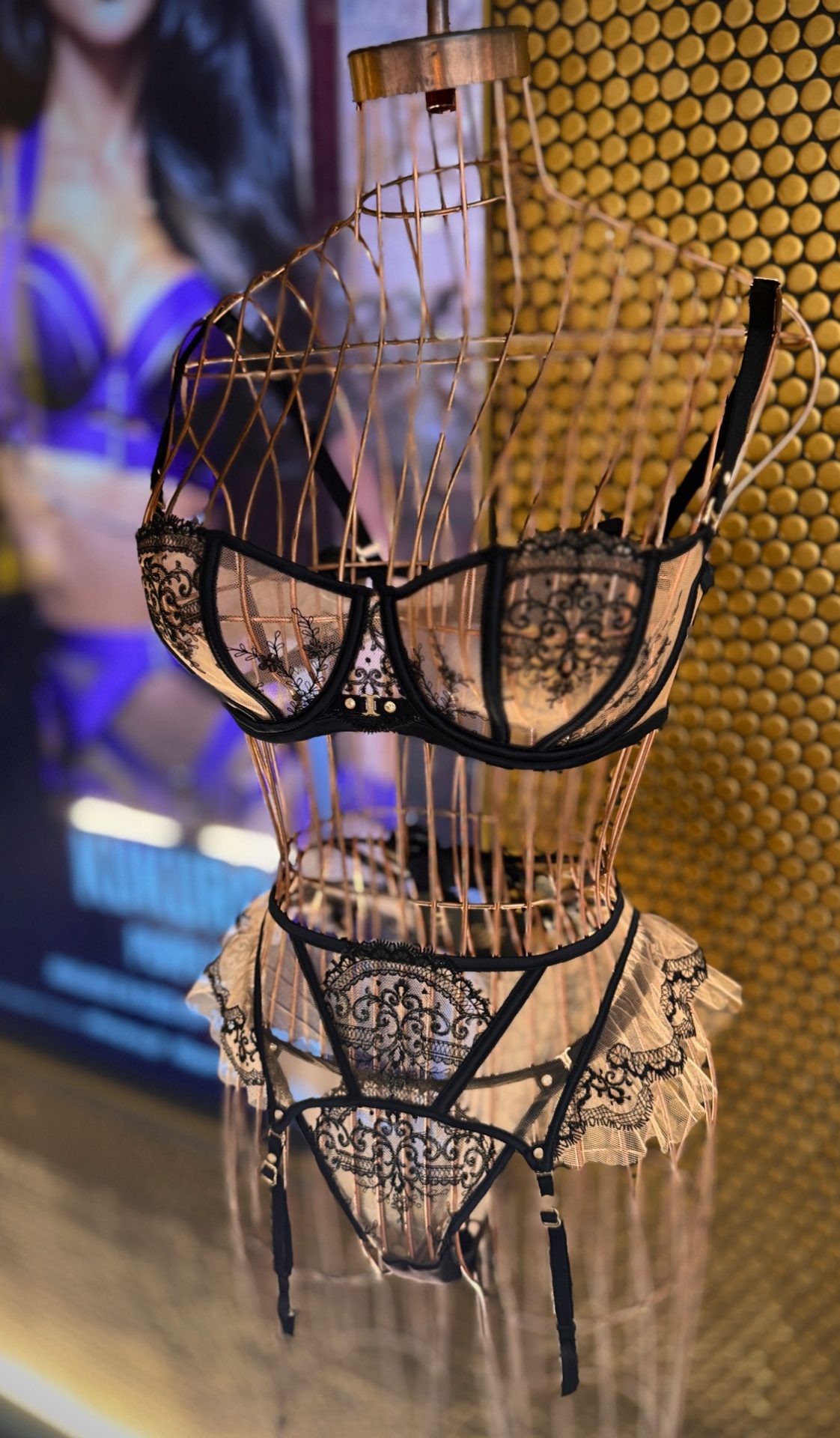 Black lace lingerie displayed on a golden wire mannequin under soft spotlights.
