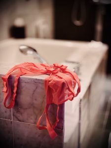 Vermilion lingerie draped over the marble edge of a bathtub, the quiet aftermath of a long night