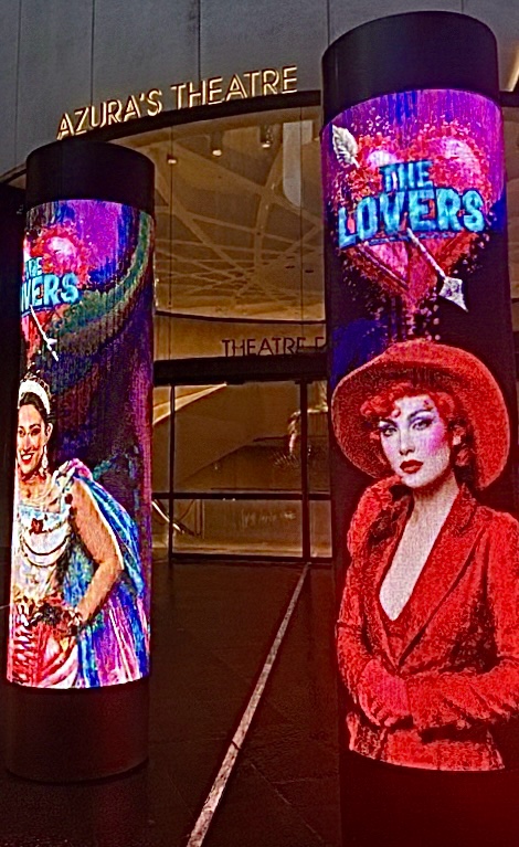 Hyperreal night scene outside “Azura’s Theatre” with neon columns and surreal portraits from The Lovers display.