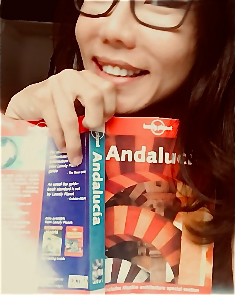 Azura smiling while holding up a Lonely Planet Andalucía guidebook.