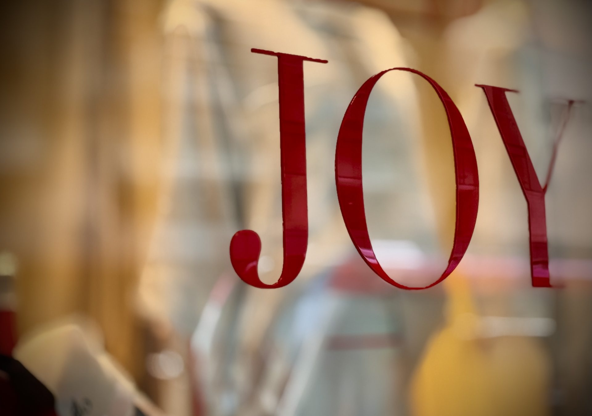 Red “JOY” lettering on a shop window with soft golden light behind it.