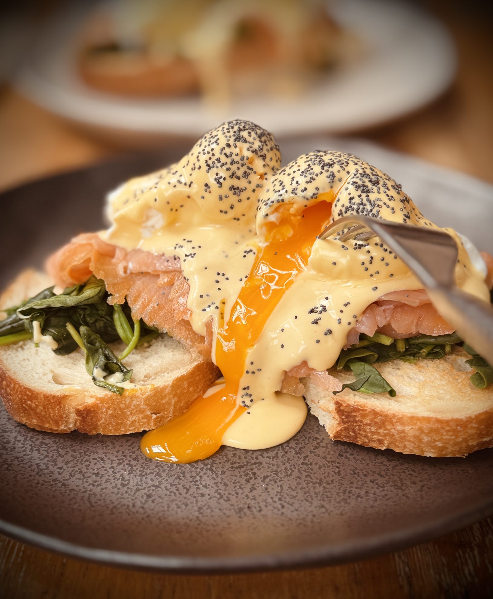 Close-up of eggs Benedict with salmon and spinach, yolk dripping onto the plate.