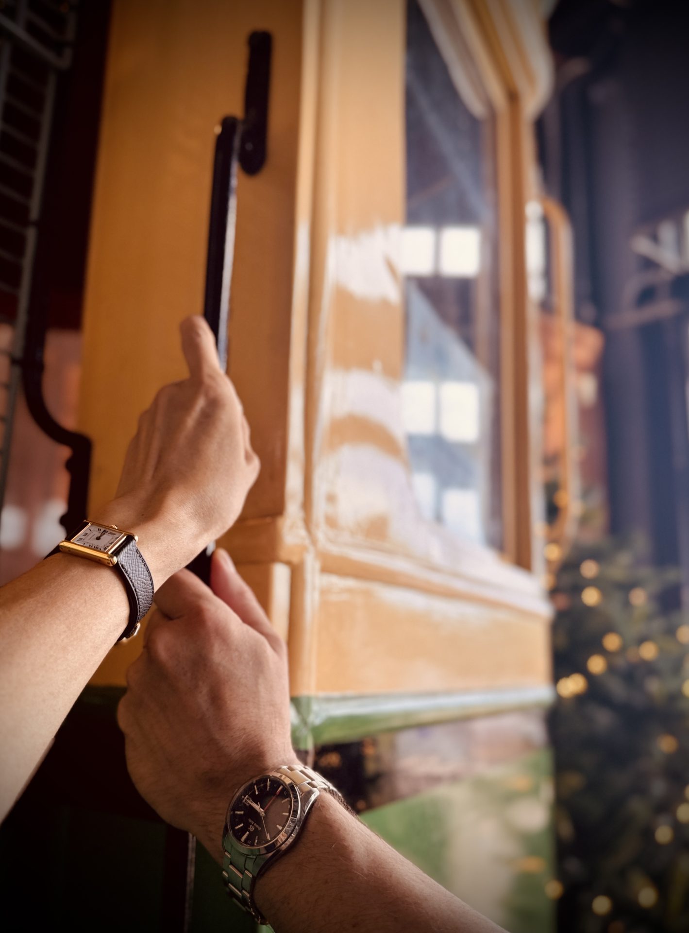 Two hands wearing watches opening the handle of a vintage tram door.