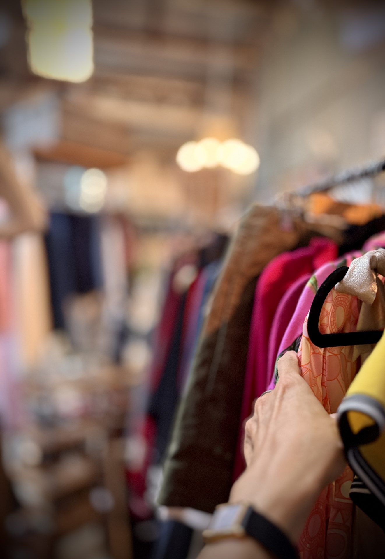 Hand sliding across clothing on a colourful op-shop rack.