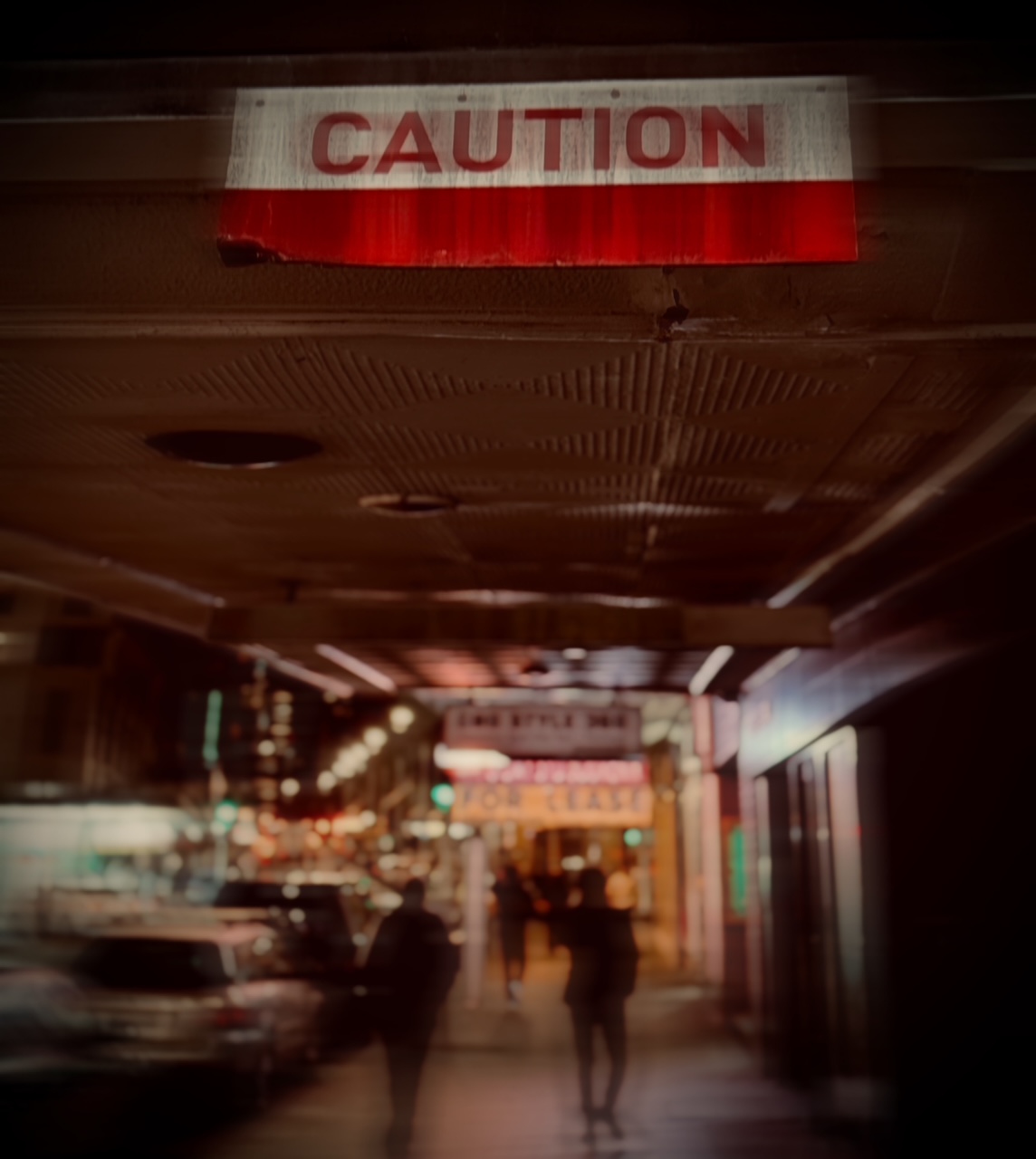 Blurred night street in Sydney with a glowing red CAUTION sign hanging above pedestrians.