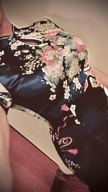 Floral cheongsam (qipao) selfie in warm indoor light, cropped torso view. 