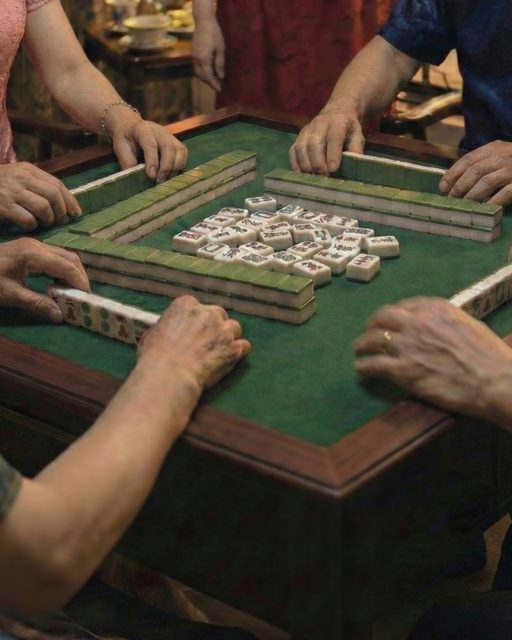 Hands gathered around a green mahjong table arranging tiles during a Lunar New Year family game.
