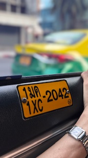 Close-up of a yellow Thai taxi license plate reading 1XC-2042, photographed from inside the same vehicle.