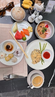 Top-down view of a table set with coffee, tropical fruit, eggs, dim sum, and pastries.