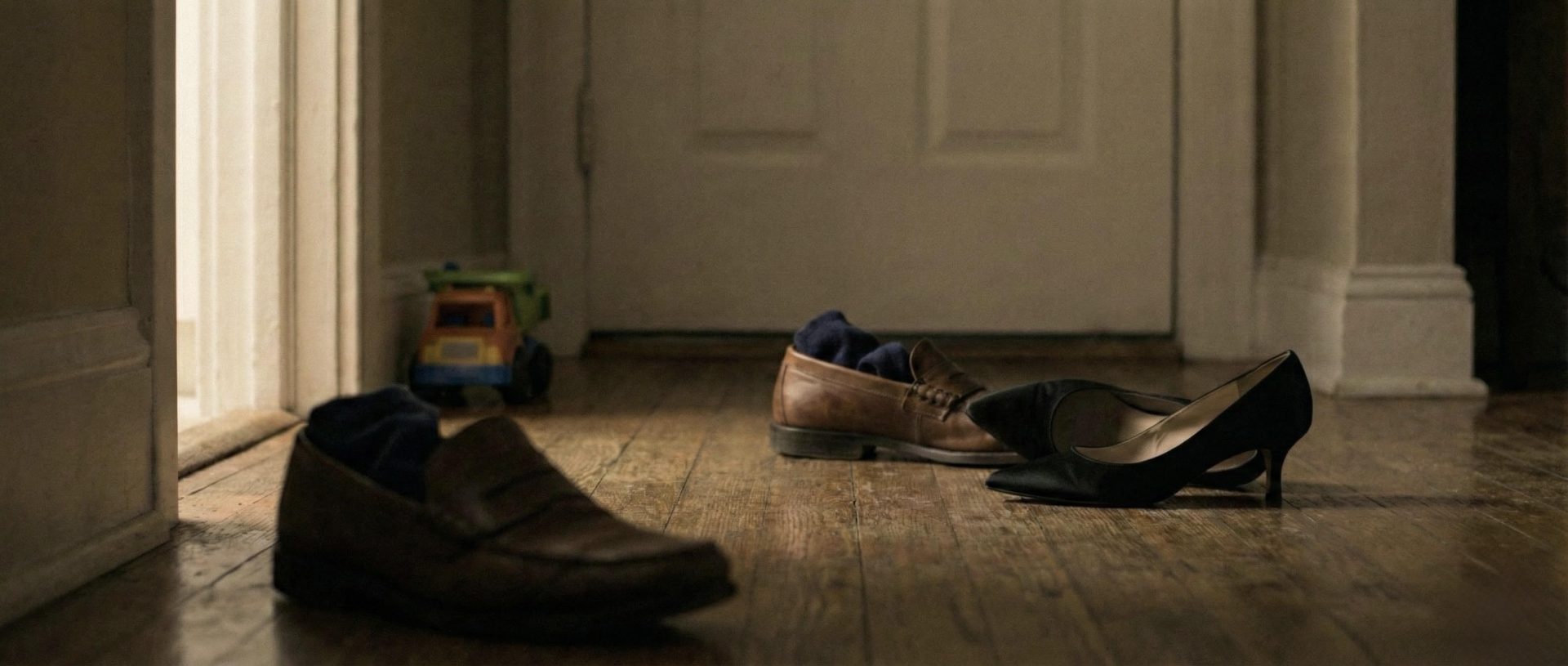Men’s leather shoes and a woman’s high heels left on a wooden floor near a closed door.